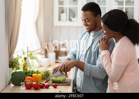 Cooking Together. Portrait of happy affectionate black couple preparing lunch in kitchen Stock Photo