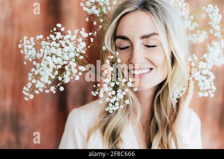 Close-up portrait of charming happy woman laughing with closed eyes in pleasure in spring mood with gypsophila flowers on her head. Portrait of a woma Stock Photo
