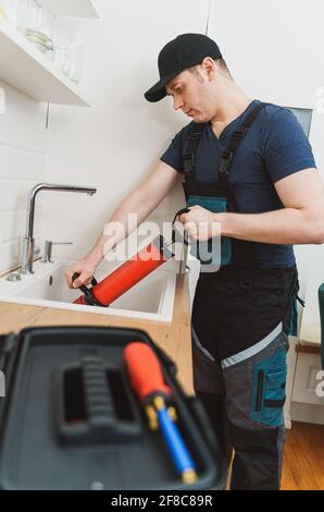 Plumber unclogging kitchen sink with professional force pump cleaner. Stock Photo