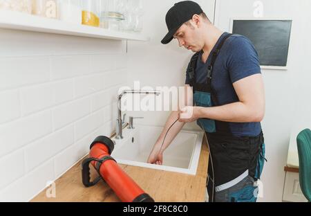 Plumber using drain snake to unclog kitchen sink. Stock Photo