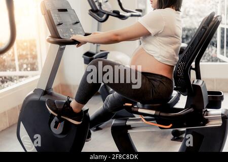 Active pregnant woman exercise in fitness center at yoga room. The young expecting mother holding baby in pregnant belly. Maternity prenatal care and Stock Photo