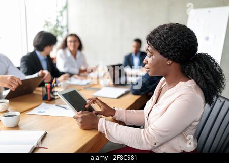 Black Businesswoman Using Digital Tablet Sitting During Corporate Meeting Indoor Stock Photo