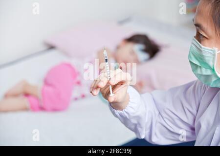 The doctor preparing an injection for a little asian girl, doctor  hand with medical syringe, shallow depth of field (DOF)  hand holding syringe in fo Stock Photo