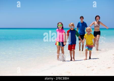 Family summer vacation. Parent and kids on tropical beach. Mother and children playing on island ocean shore running on white sand in clear water.