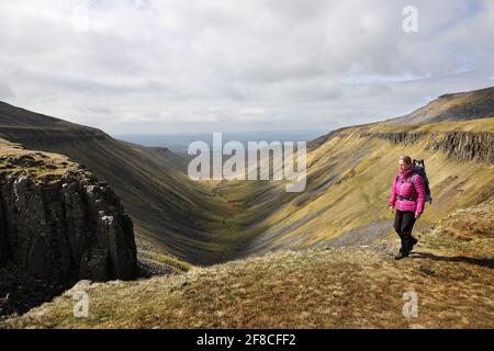 High Cup Nick, Dufton, Cumbria, UK. 13th April 2021. UK Weather.  A walker enjoys some far reaching views as she walks above the spectacular geological feature of High Cup Nick in the North Pennines as cloud builds over the Eden valley in Cumbria. Credit: David Forster/Alamy Live News Stock Photo