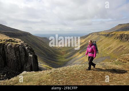 High Cup Nick, Dufton, Cumbria, UK. 13th April 2021. UK Weather.  A walker enjoys some far reaching views as she walks above the spectacular geological feature of High Cup Nick in the North Pennines as cloud builds over the Eden valley in Cumbria. Credit: David Forster/Alamy Live News Stock Photo