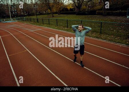 Caucasian male athlete holding hands behind head walking on tracking field Stock Photo
