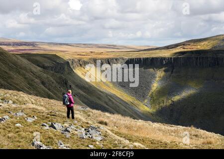 High Cup Nick, Dufton, Cumbria, UK. 13th April 2021. UK Weather.  A walker enjoys some far reaching views as she walks above the spectacular geological feature of High Cup Nick in the North Pennines as cloud builds over the Eden valley in Cumbria. Credit: David Forster/Alamy Live News Stock Photo