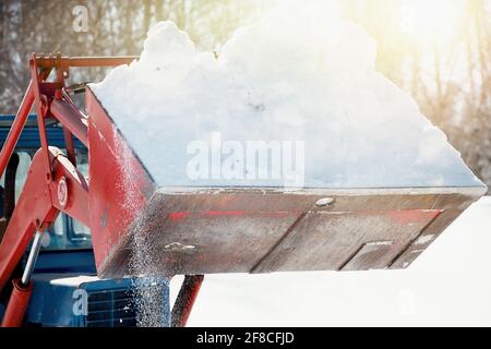 Tractor in a bucket to take out the snow. Clearing the territory from the effects of snowfall. The excavator clears the streets of snow. Stock Photo