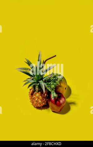 Mini pineapple, mango and apple on a solid yellow background Stock Photo