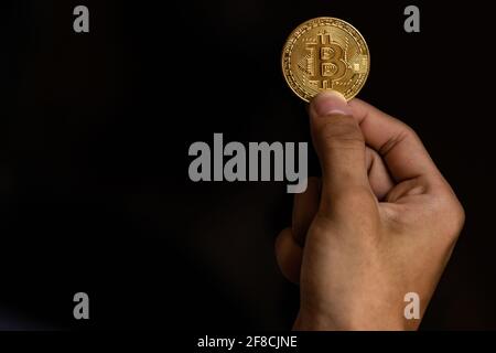 Close up one golden coin with the bitcoin symbol in hand. Young hand holding cryptocurrency coin, Money coins digital, BTC Stock Photo
