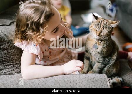 Little girl playing with her cat on the couch in the living room