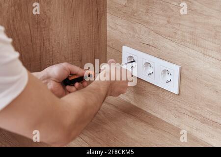 Electrician hands mounting socket in the wall. Socket installation Stock Photo