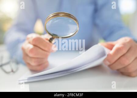 Businessman reading documents with magnifying glass concept for analyzing a finance agreement or legal contract Stock Photo
