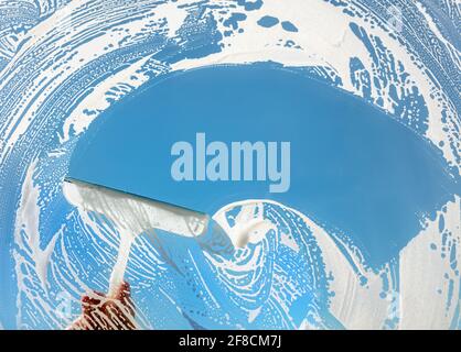 Window cleaner using a squeegee to wash a window with clear blue sky Stock Photo