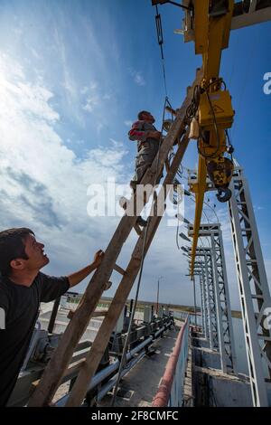 Kazakhstan, Shardara water storage dam. Asian (Uzbek) electrician workers fixing winch. Renovation of water shutter lifting device. Stock Photo