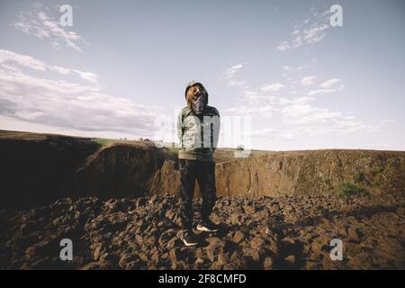 Boy in Camouflage Hoodie and Bandit mask Stands on Basalt Mesa Stock Photo