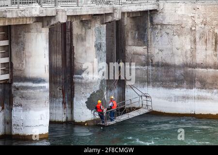 Two maintenance engineers or technicians in suspended cradle watching Shardara river dam. Supervising of concrete quality. Stock Photo