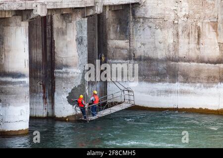 Two maintenance engineers or technicians in suspended cradle watching Shardara river dam. Supervising of concrete quality Stock Photo