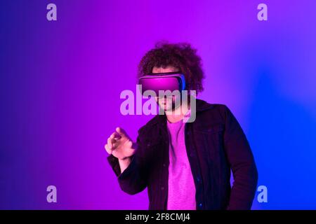 Hipster young man using virtual reality headset over blue purple Stock Photo