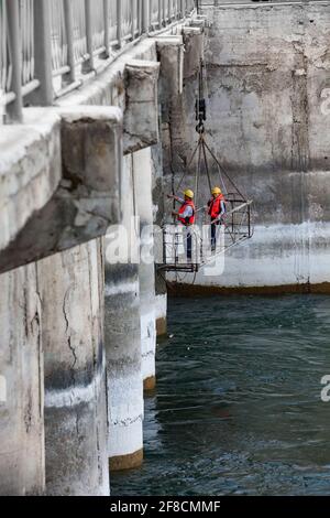 Two maintenance engineers in suspended cradle watching Shardara river dam. Supervising of concrete quality. Stock Photo