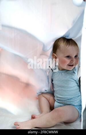 portrait of baby girl hiding under curtains Stock Photo