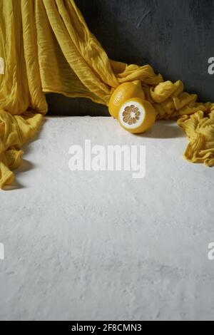 Two lemons and a yellow draped fabric on a white and gray background Stock Photo