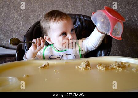 baby girl pours porridge from a bowl Stock Photo