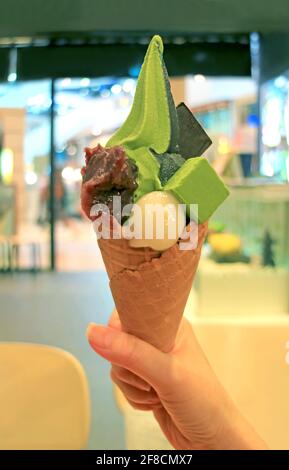 Hand Holding a Green Tea Soft Serve Ice Cream Cone with Japanese Dessert Anmitsu Stock Photo