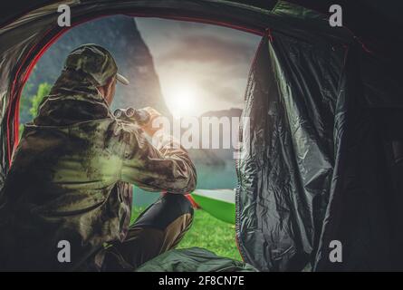 Caucasian Hunter in His 40s Spotting Wildlife Using Professional Binoculars Straight From His Hunting Spot Tent. Hunting Season Theme. Stock Photo
