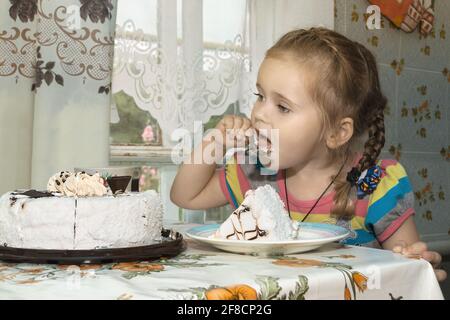 Little cute girl is eating a cake while sitting at the kitchen table in an old country house. Selective focus Stock Photo