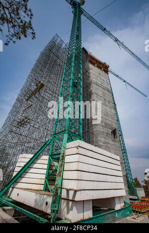 Construction of modern high-rise ski-jump in Shchuchinsk city, Kazakhstan. Concrete tower, scaffoldings and construction cranes on blue sky. Stock Photo