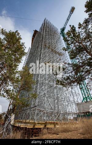 Construction of modern high-rise ski-jump in Shchuchinsk city, Kazakhstan. Scaffolding and concrete tower and pine-trees. Stock Photo