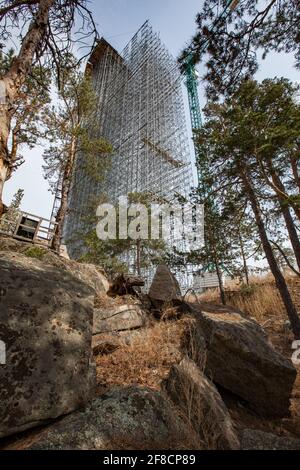 Construction of modern high-rise ski-jump in Shchuchinsk city, Kazakhstan. Scaffolding, concrete tower and pine-trees Stock Photo