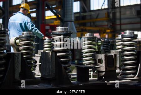 Kazakhstan, Nur-sultan locomotive-building plant. Close-up of damper spring. Worker on background, blurred. Stock Photo