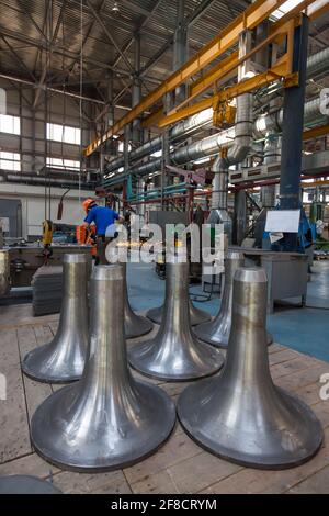 Kazakhstan, Nur-sultan. Locomotive-building plant workshop. Wagon buffer close-up on foreground and worker with angle grinder and sparks. Stock Photo