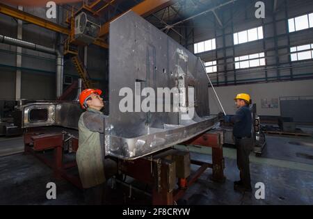 Kazakhstan, Nur-sultan. Locomotive-building plant workshop. Two workers take a locomotive's cabin part. Stock Photo