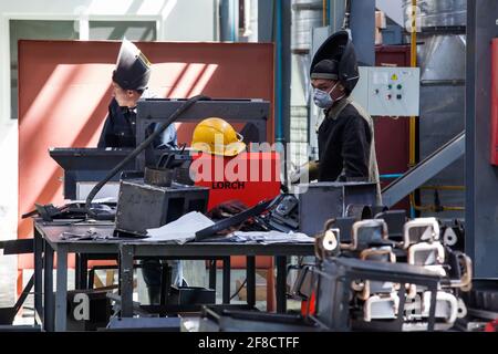 Locomotive-building plant. Two Asian welder workers and apparatus in workshop. Beautiful daylight and shadow. Stock Photo