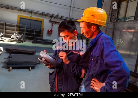 Locomotive-building plant. Two Asian workers programming CNC machine. Stock Photo