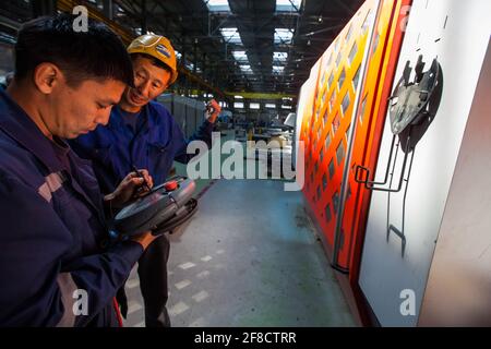 Locomotive-building plant. Two Asian workers programming CNC machine. Stock Photo