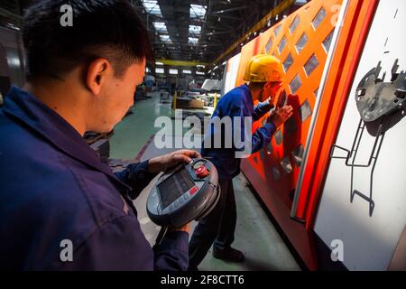 Locomotive-building plant. Two Asian workers programming CNC machine. Stock Photo