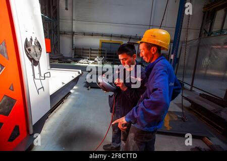 Locomotive-building plant. Two Asian workers programming CNC machine. Stock Photo