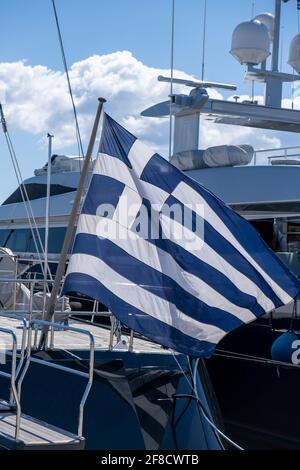 Greek flag on a luxury boat anchored in a marina in Greece. Blue white color flag waving on yacht stern. Blue sky background, close up view. Stock Photo