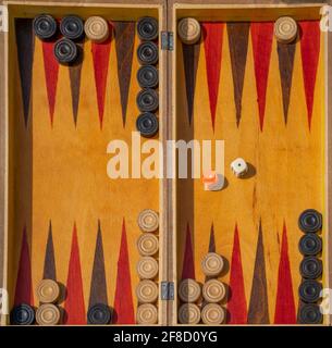 A wooden backgammon board marked brown and red, with wooden game pieces. Stock Photo