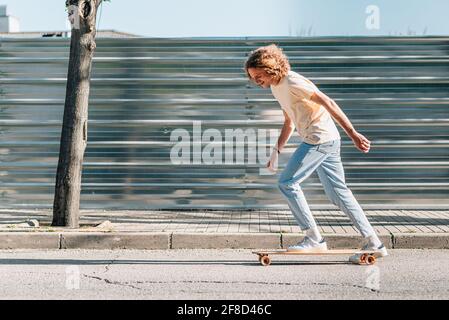 caucasian thin man with curly and long red hair skating in the city. He is dressing casual clothes. Stock Photo