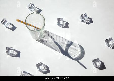 An empty glass with ice and big sun shadow of glass on a white background. Solar photography. Top view, hot summer and drink concept. Stock Photo