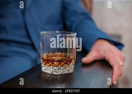 A glass of whiskey on a wooden stand, a man sits in the background Stock Photo