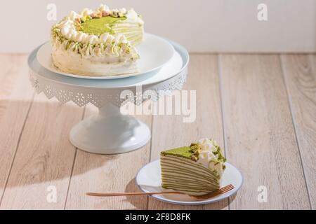 Matcha Mille Crepe Cake Presented On A Cake Holder With A Slice On A Plate Stock Photo