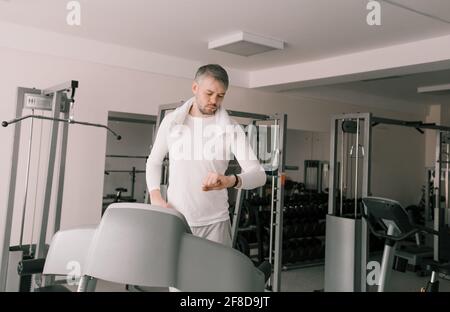 a man stands on a treadmill and carefully looks at the clock after a cardio workout. Taking care of your body.