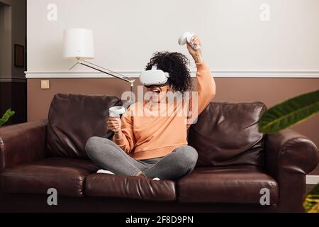 Excited female gamer using virtual reality headset while sitting in room Stock Photo